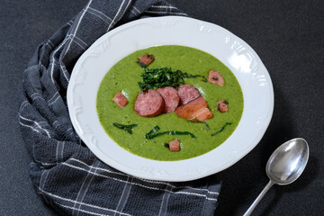 Delicious green soup with sausage, cabbage and bancon on a white plate