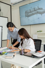 Obraz premium Two Asian women working together in a bright, modern studio.while using a laptop and smartphone. The creative workspace is filled with colorful samples for seasonal palette selection.