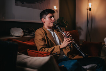 Fototapeta premium A man in a warm-toned room is playing a clarinet, focusing passionately on his music. The setting appears intimate and comfortable, suggesting a mood of relaxation and musical expression.