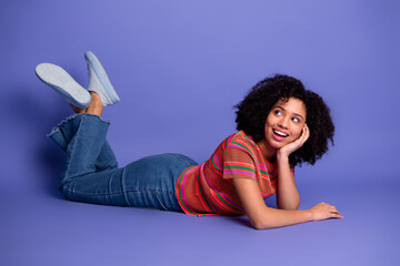 Smiling young woman lying on violet background wearing casual attire and feeling cheerful...