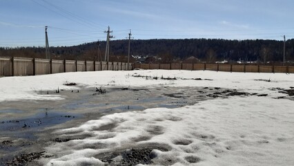 Winter landscape with melting snow and puddles under clear blue sky in rural area