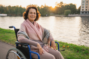 Happy senior woman in wheelchair smiling enjoying freedom walking on road in city park outdoor. Old cheerful positive woman in chair for people with disability. Disability disease rehabilitation