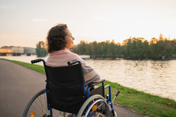 Sad senior woman sitting in wheelchair walking on road in city outdoor, back view. Old paralyzed lady in chair for people with disability feel depressed. Lonely elderly sick woman sits on wheelchair
