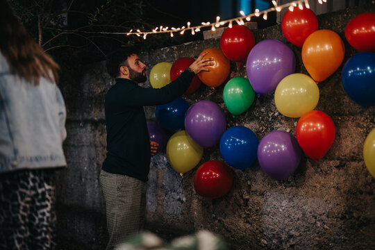A man places balloons on a wall decoration at an outdoor birthday party during evening festivities.