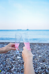 Two Hands Holding a Glass of Pink Sparkling Drink Against the Sea Background