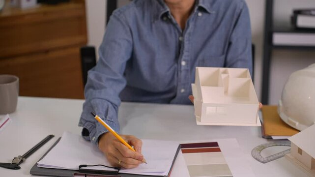 Closeup of woman architect sketching floor plans with house model on desk at minimalist workplace