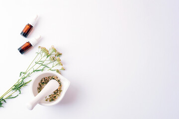 Herbal cosmetic set with essential oil bottles, dried yarrow flowers and mortar on white background. Top view, flat lay, copy space