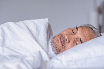 senior man laying comfortable under a white blanket,resting,bedtime deep sleeping in a cozy...