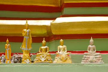 Small buddha icons line a shelf on a colorful green, red and gold temple stupa