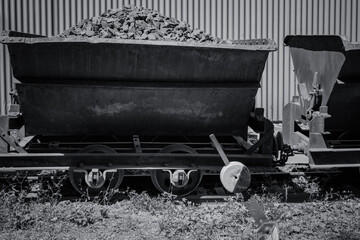 Rusty train carts filled with stones sit abandoned against a weathered industrial backdrop in the...