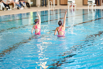 Two women performing synchronized swimming in a pool, showcasing coordination, grace, and...