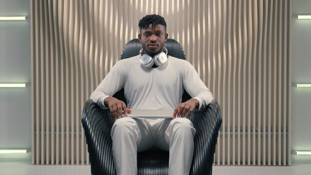 Young African American man guy male put on headphones opening laptop indoors in futuristic room looking at screen concentrated in modern cyberspace online internet gaming hacking programming futurism