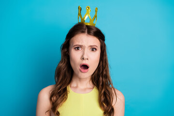 Adorable Woman in Yellow Dress with Golden Crown Against Bright Blue Background Showing Surprised...