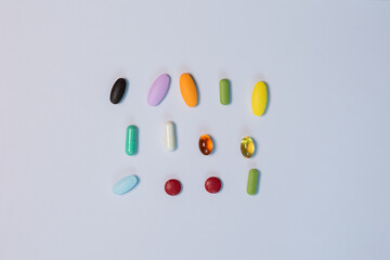 Close-up top-view of assorted colorful pills and supplements arranged neatly on white background. Lay flat composition highlights health care, daily vitamins with clean, minimal presentation.