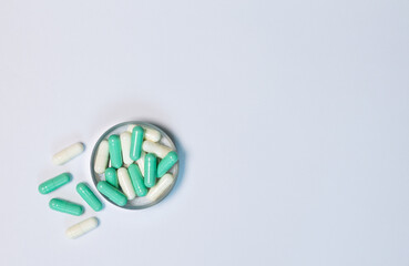 Close-up top-view of green and white capsule pills in a metal container on white background. Lay flat composition shows pharmaceutical use, healthcare concepts, and clean, medical product.