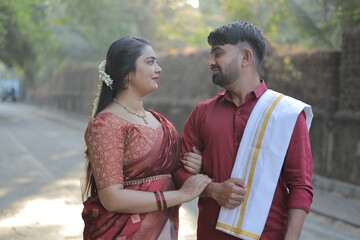 A beautiful South Indian couple dressed in elegant traditional attire walking hand in hand along a...