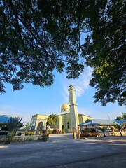 Sunlight streams through the trees, casting a serene glow on the pale yellow facade.  Perfect morning.