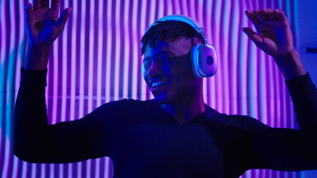 African American man guy male dancing DJ mix listening audio song sound music in modern wireless headphones dance having fun at house party with neon light modern movements relaxing freedom moving