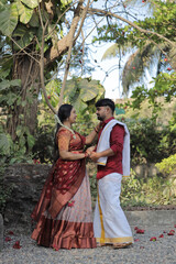 A beautiful South Indian couple dressed in elegant traditional attire walking hand in hand along a...
