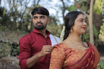 A beautiful South Indian couple dressed in elegant traditional attire walking hand in hand along a...