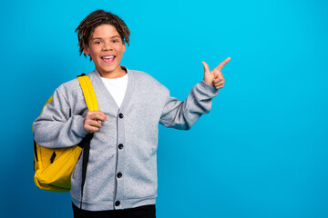 Excited schoolboy with backpack making cheerful gesture against blue background illustrating...