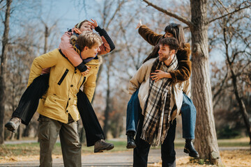 Two happy couples having fun outdoors, a piggyback ride among trees in the fall. This image shows...