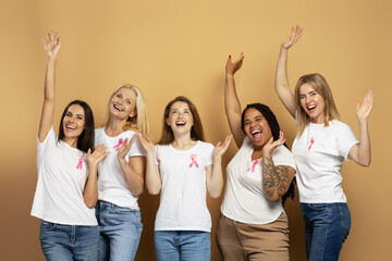 Happy women raising hands and celebrating breast cancer awareness