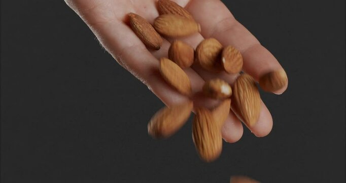 Almonds falling from a hand on a dark background.