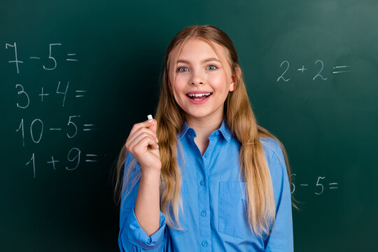 Happy schoolgirl holding chalk in front of chalkboard with math problems, expressing confidence and enthusiasm for learning - Powered by Adobe