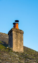 An old traditional stone chimney on a mossy slate roof under a clear sky.