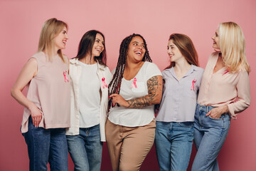 Five smiling women wearing pink ribbons supporting breast cancer awareness