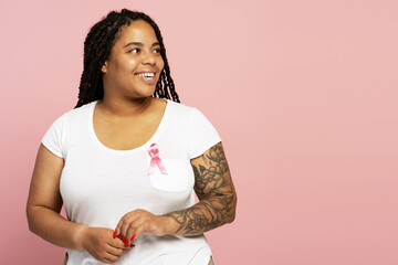 Smiling woman wearing pink ribbon is looking away on pink background