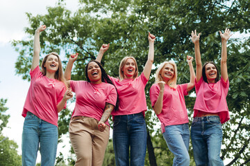 Smiling women wearing pink raising arms for breast cancer awareness