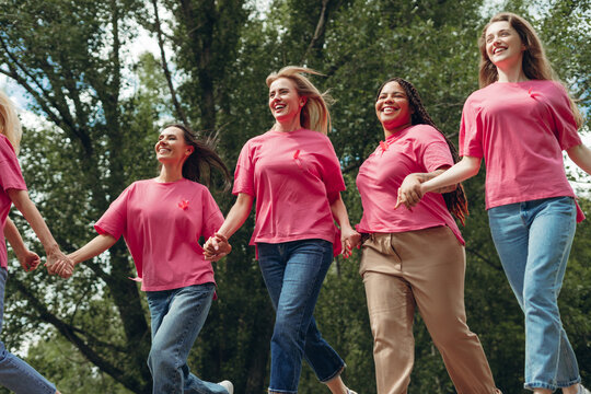 Diverse women running for breast cancer awareness, holding hands and smiling - Powered by Adobe
