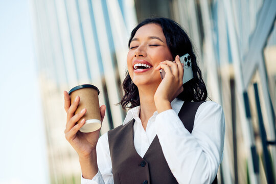 Confident businesswoman enjoying outdoor work call holding coffee, reflecting modern urban lifestyle and success
