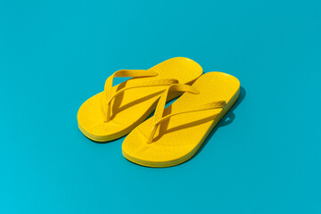 Pair of yellow beach flip-flops on turquoise blue background central composition. Minimalist flat...
