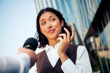 Confident young businesswoman being interviewed outdoors in the city with urban buildings in the...