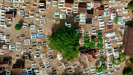Overhead aerial view of a densely packed traditional Indonesian cemetery with colorful graves and a central green tree