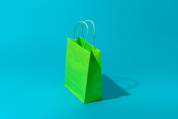 Green shopping bag standing on the turquoise blue background with copy space. Minimalist photo of paper bag with harsh shadow central composition. Summer sale and shopping concepts.