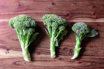 Three heads of broccoli lined up on a wood cutting board