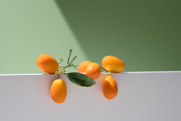 Kumquats naranjas chinas pequeñas sobre un soporte blanco y fondo verde	