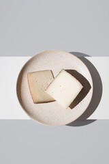 Dos trozos de queso de oveja curado y de cabra sobre un plato de cerámica y fondo gris. Vista superior