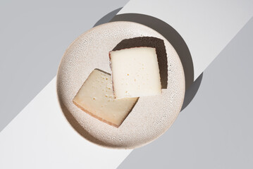 Dos trozos de queso de oveja curado y de cabra sobre un plato de cerámica y fondo gris. Vista superior