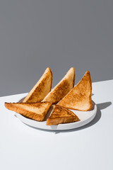 Triángulos de pan tostado dorados para sándwiches en un plato blanco sobre un fondo gris