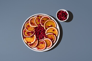 Rodajas de naranja sanguina y semillas de granada en un plato blanco sobre un fondo azul. Vista...