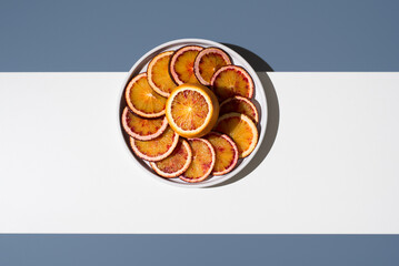 Rodajas de naranjas sanguinas en un plato blanco sobre un fondo blanco y azul. Vista superior