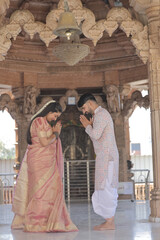 An Indian couple poses gracefully at a beautifully carved Hindu temple. The woman is wearing a rich...