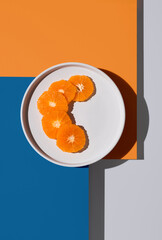 Rodajas de mandarina en un plato blanco sobre fondo naranja y azul. Vista superior