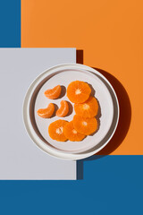 Rodajas y gajos de mandarina en un plato blanco sobre fondo naranja y azul. Vista superior