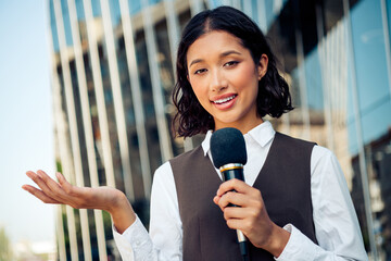 Confident young businesswoman with microphone in urban setting presenting professionally with...